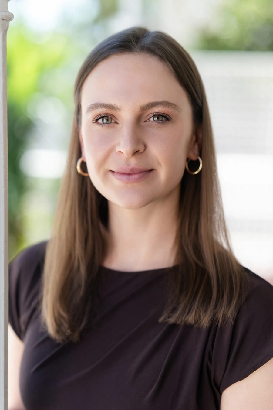 Close portrait of the practice owner on the veranda, a white column and garden behind her