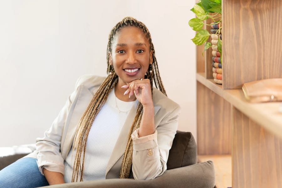 Psychotherapist seated in a cream blazer beside a timber bookshelf, chin resting on her hand