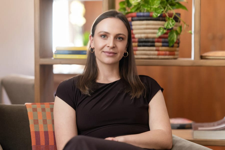 The practice owner seated in her consulting room, bookshelves and plants behind her
