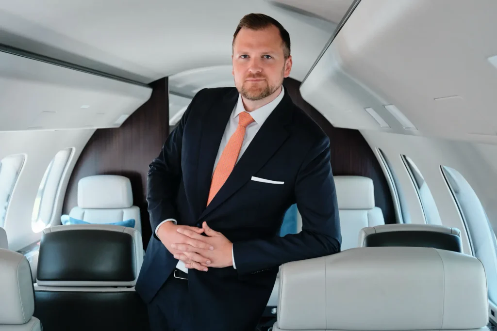VistaJet executive in a suit, leaning on a seat inside the private aircraft cabin, looking at camera