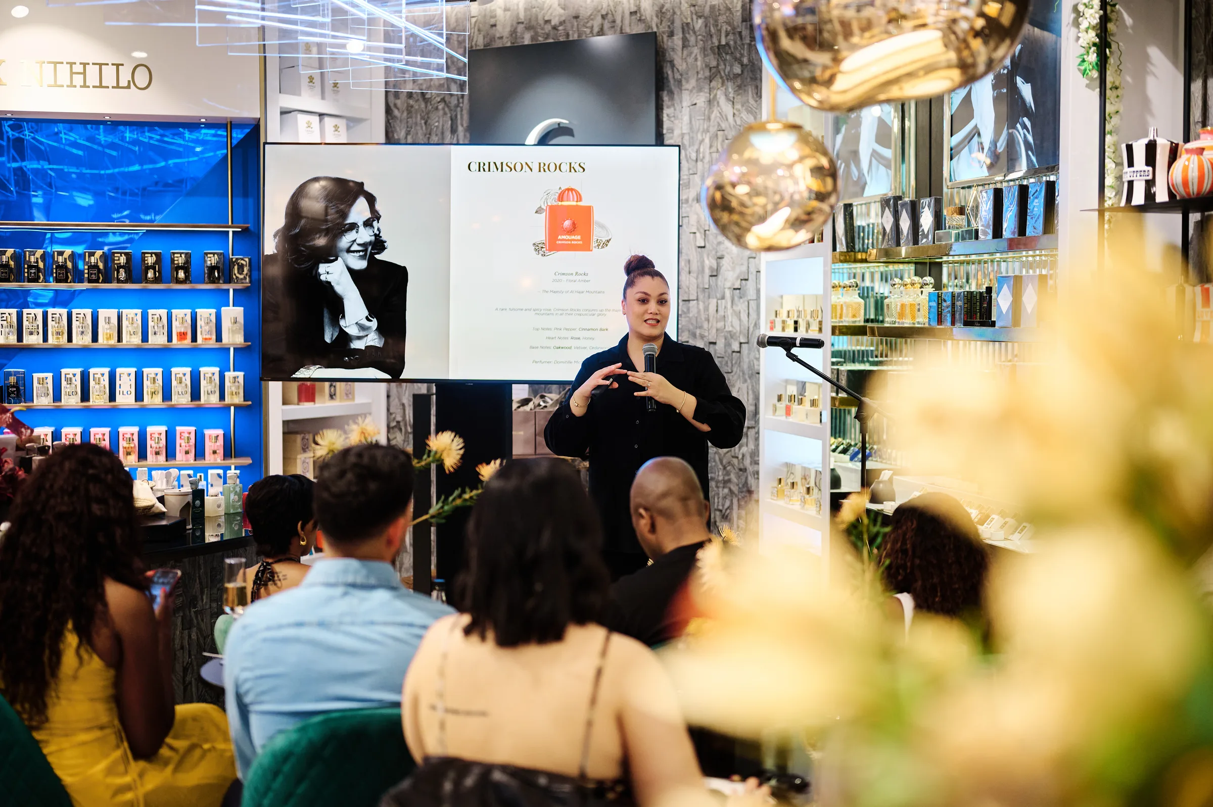 Presenter addressing seated guests among the shelves at a retail fragrance launch, Cape Town