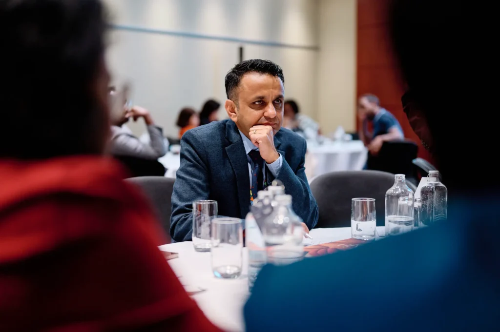 A candid shot of a delegate listening intently during a conference session, capturing the atmosphere of the event.