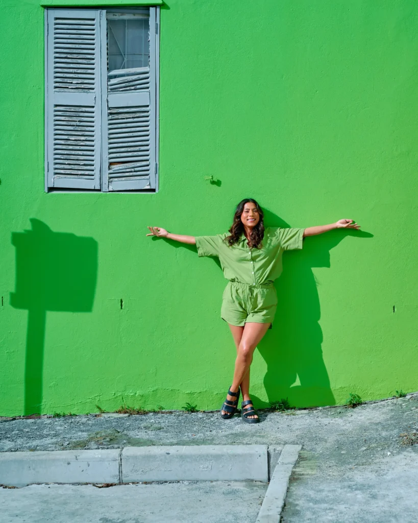 A full-body vertical branding portrait with open arms against a vibrant green Bo-Kaap wall.