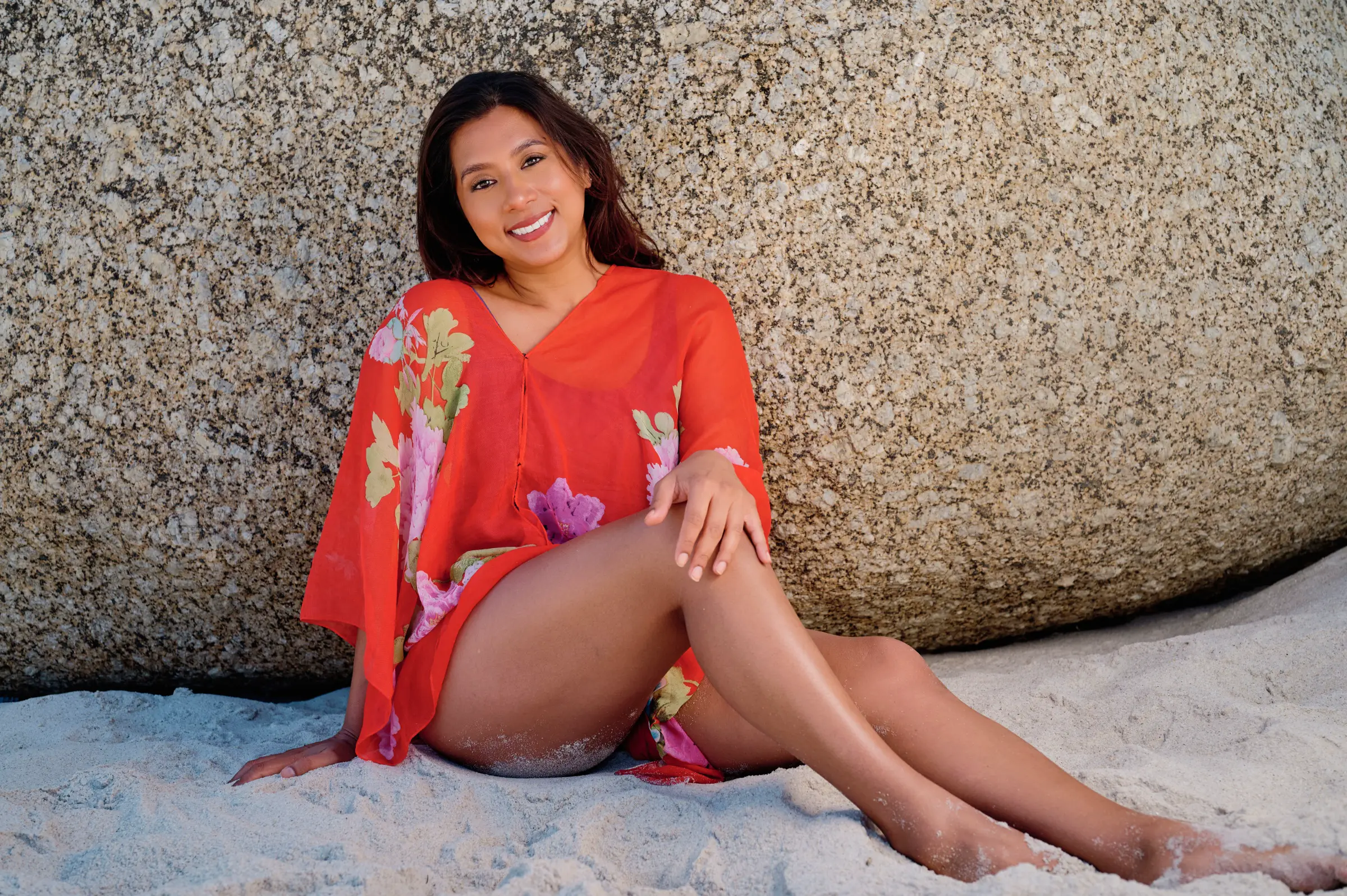 A professional environmental personal branding portrait of a female leader in red attire, leaning against a granite boulder in Cape Town, conveying visual authority and confidence.